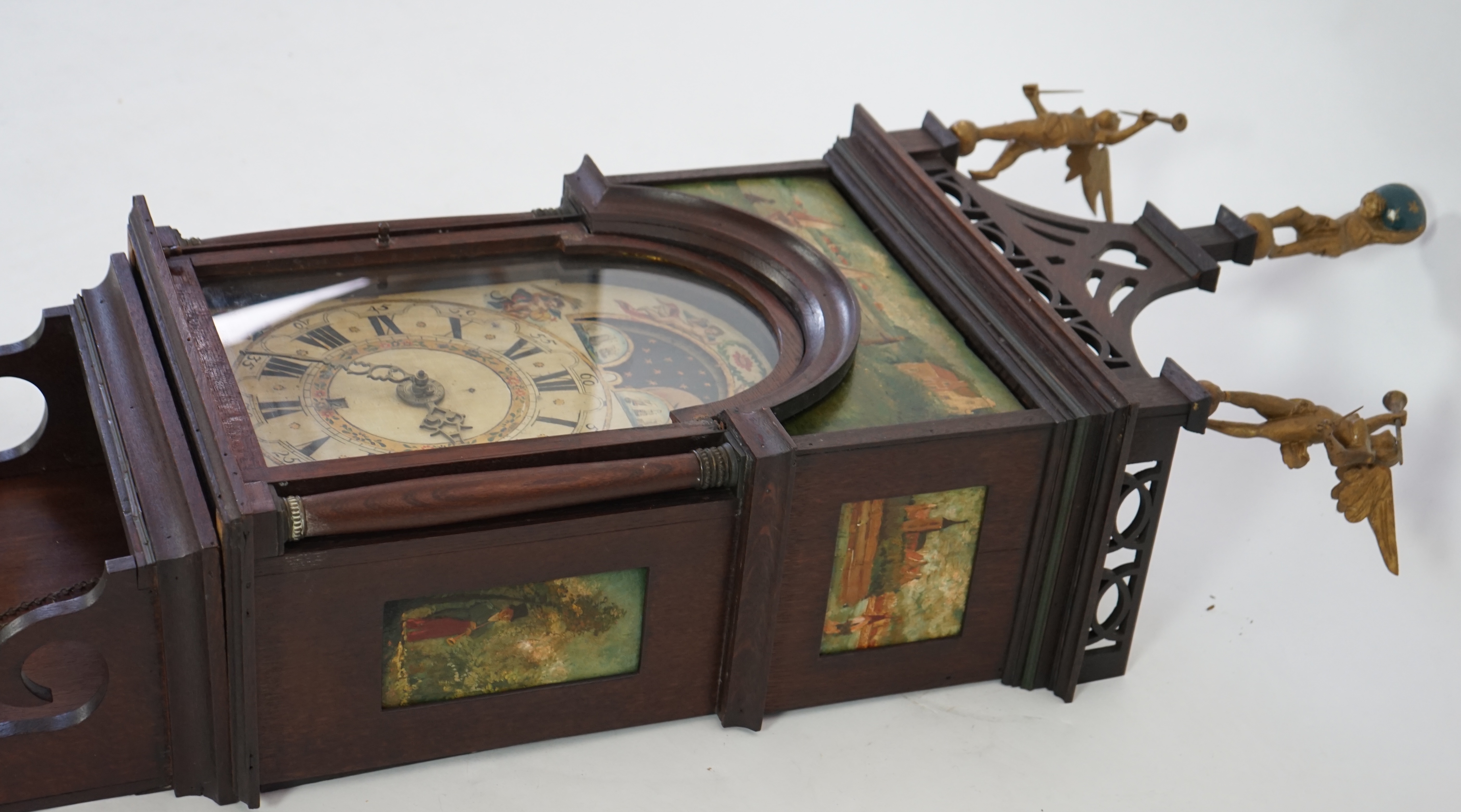 A late 18th century Dutch Frisian Staart oak eight day wall clock, with atlas and angel finials, hood painted with a Dutch riverscape and painted arched dial with moonphase, date aperture and alarm indicator, 47cm wide,
